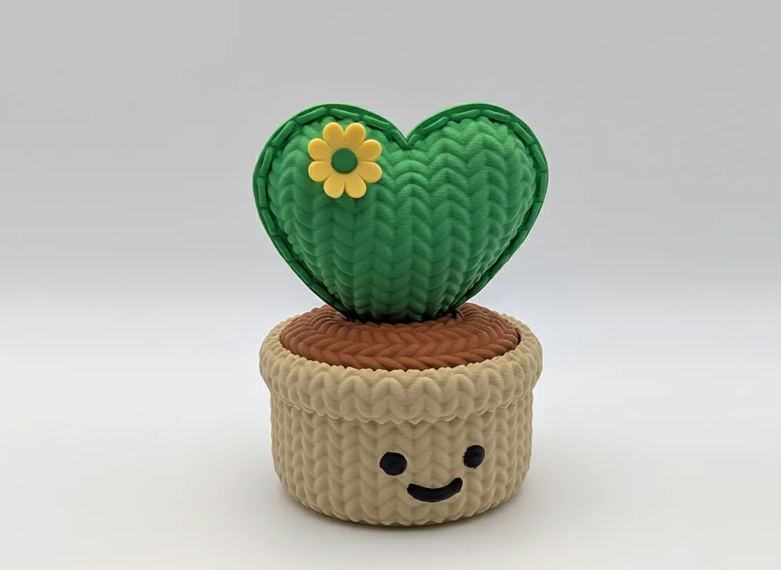 Heart-shaped green knitted cactus with a yellow flower on a beige pot against a white background